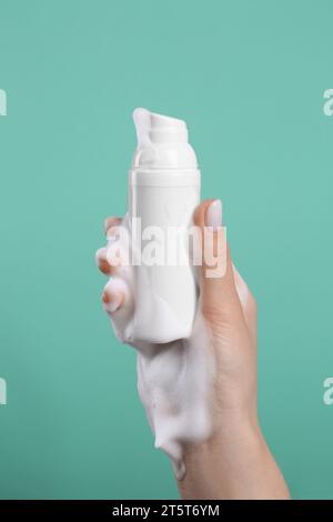 Frau mit Schaum auf der Hand hält Flasche Hautreiniger vor grünem Hintergrund, Nahaufnahme. Kosmetisches Mittel Stockfoto