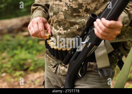 Mann mit Gewehr, der draußen Patronen aus dem Gürtel nimmt, Nahaufnahme. Jagdsaison Stockfoto