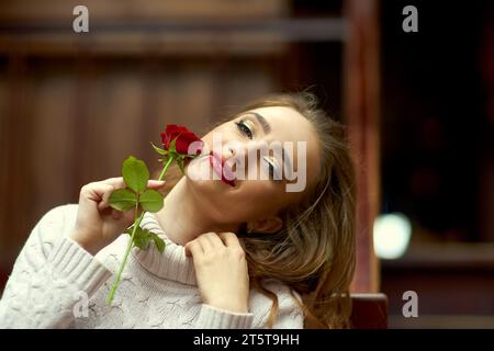 Die süße junge Gen Z-Frau mit hellem Make-up hält eine Rose an der Wange und genießt ein Geschenk von ihrem Mann. Das Konzept, einen Freund zu treffen, Valentine' Stockfoto