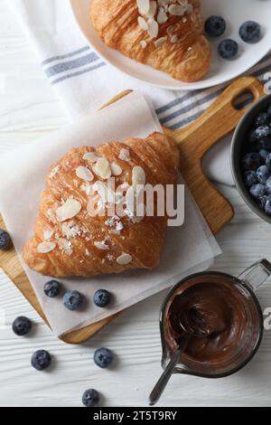 Köstliche Croissants mit Mandelflocken, Schokolade und Heidelbeeren serviert auf weißem Holztisch, flach gelegt Stockfoto