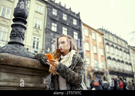 Stilvoller Tourist in der kalten Jahreszeit in der Stadt sucht nach Wegbeschreibungen auf einem Handy. Warten auf einen Freund oder Freund, um die Stadt zu erkunden. Trav Stockfoto