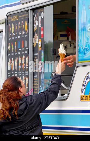 Ein zufriedener Kunde nimmt ein frisch zubereitetes 99 Flake Eis vom Verkäufer an der Serviertheke eines Eiswagens während eines hektischen lokalen Lebensmittelfestivals an. Stockfoto