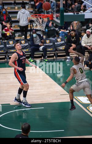 College-Basketballspieler, der während der NCAA-Action einen Layup am Rand beendet, werden mit scharfen Details und dynamischen Bewegungen auf dem Hallenplatz erfasst. Stockfoto
