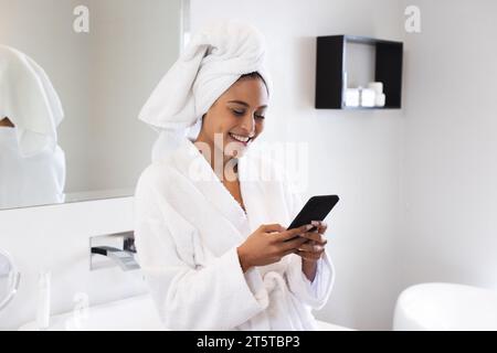 Glückliche Frau mit Bademantel und Smartphone im Badezimmer Stockfoto