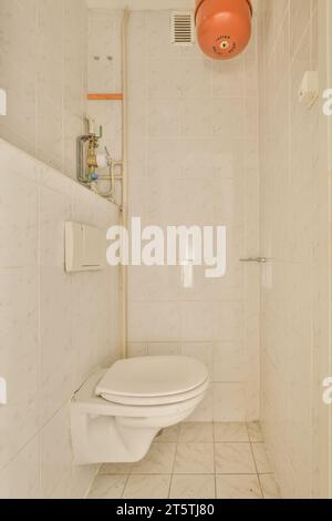 Ein Badezimmer mit Toilette und einer orangen Kugel, die an der Wand vor der Toilette hängt, besteht aus weißen Marmorfliesen Stockfoto