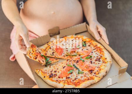 Eine schwangere Frau genießt ein Stück Pizza und genießt einen Moment der Genussfreude, während sie ihr Verlangen nach einer köstlichen, wohltuenden Leckerei befriedigt. Begeistert Stockfoto