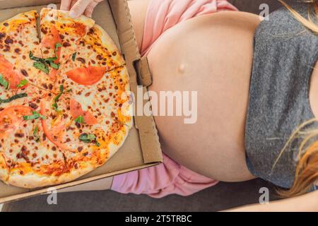 Eine schwangere Frau genießt ein Stück Pizza und genießt einen Moment der Genussfreude, während sie ihr Verlangen nach einer köstlichen, wohltuenden Leckerei befriedigt. Begeistert Stockfoto