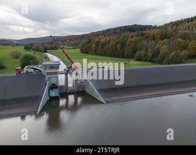 PRODUKTION - 01. November 2023, Hessen, Bad Soden-Salmünster: Ein Bagger steht auf dem Wehr des Kinzigtaler Damms (Luftaufnahme mit Drohne). Nach dem Austausch der defekten Dammtore sollte der Tank in den kommenden Monaten wieder mit Wasser gefüllt werden. (Zu dpa 'Arbeiten am Kinzig-Damm bald abgeschlossen - Staudamm kann beginnen') Foto: Boris Roessler/dpa Stockfoto