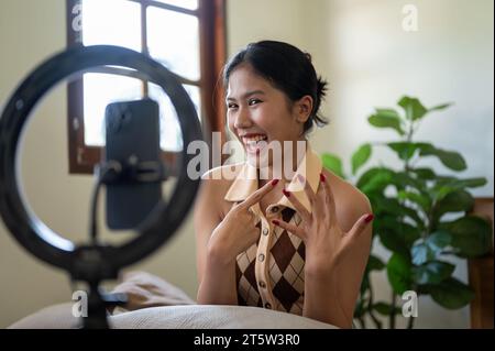 Eine attraktive junge asiatische Influencerin oder Beauty-Bloggerin rezensiert oder spricht mit der Kamera und nimmt ihr Video zu Hause auf. Stockfoto