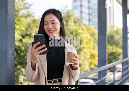 Eine wunderschöne asiatische Geschäftsfrau der Millennials reagiert auf Nachrichten auf ihrem Handy auf einem Skywalk. Städtisches Leben, Menschen und Technologiekonzepte Stockfoto