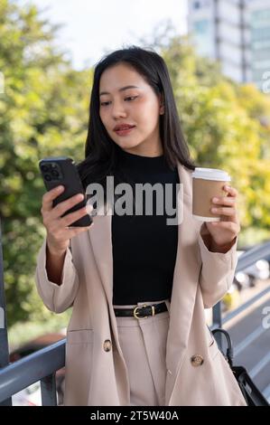 Eine wunderschöne asiatische Geschäftsfrau der Millennials reagiert auf Nachrichten auf ihrem Handy auf einem Skywalk. Städtisches Leben, Menschen und Technologiekonzepte Stockfoto