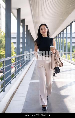 Eine selbstbewusste und wunderschöne Millennials asiatische Geschäftsfrau wird morgens arbeiten und auf einem Skywalk in der Stadt spazieren gehen. Urbanes Stadtleben und Korpora Stockfoto