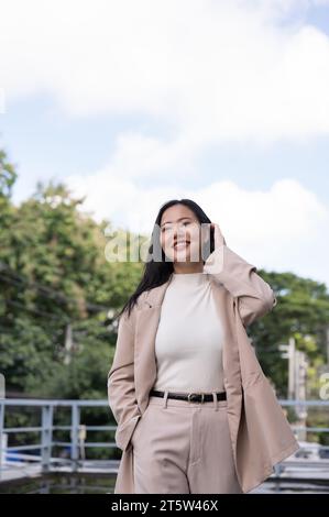 Eine schöne und fröhliche Millennials asiatische Geschäftsfrau in einem trendigen Business-Anzug spaziert an einem helleren Tag durch die Stadt. Urban City Life Konzept Stockfoto