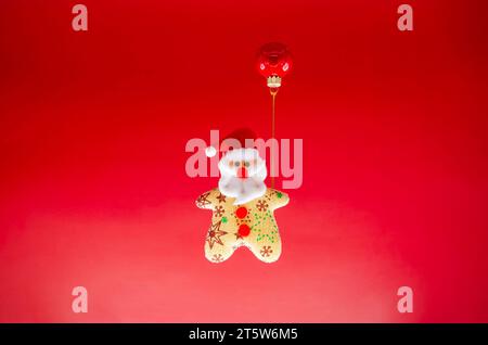 Weihnachtsschmuck mit Weihnachtsmann und roter Kugel als Ballon auf rotem Hintergrund. Minimales Urlaubskonzept. Stockfoto