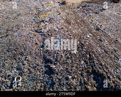 Aus der Vogelperspektive auf einer riesigen Deponie, wo Bulldozer arbeiten und LKWs neue Abfälle bringen. Riesige Vogelschwärme fliegen über die Szene. Stockfoto