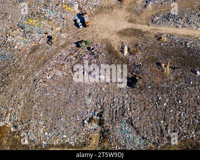 Aus der Vogelperspektive auf einer riesigen Deponie, wo Bulldozer arbeiten und LKWs neue Abfälle bringen. Riesige Vogelschwärme fliegen über die Szene. Stockfoto