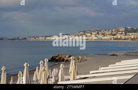 Schön, Frankreich: Blick auf den Strand mit Liegestühlen und Sonnenschirmen in Nizza. Der Strand und die Promenade des Anglais sind fast das ganze Jahr über voll. Stockfoto