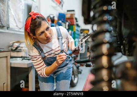 Eine Mechanikerin, die die Motorraddokumentation in der Garage ausfüllt Stockfoto