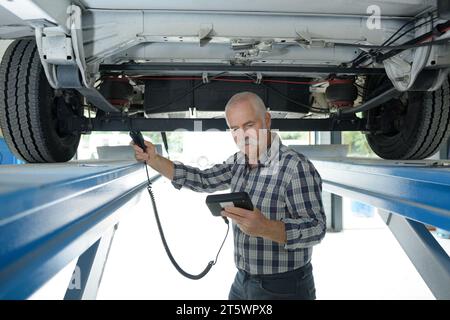 Der leitende Mechaniker überprüft den technischen Zustand unter einem Auto Stockfoto