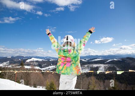 Ein erwachsenes Mädchen, mit ausgestreckten Armen, bewundert die Berglandschaft und genießt das sonnige Winterwetter. Interessanter aktiver Winterurlaub, Skigebiete Stockfoto