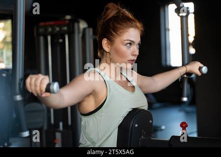 Eine junge Frau wird in einem Moment der Konzentration und des Hingabe gefangen, während sie im Fitnessstudio Krafttraining macht und die Intensität und den foc zeigt Stockfoto