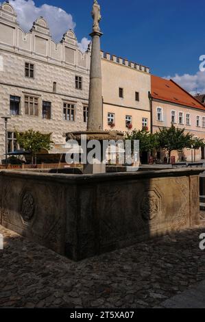 Brunnen in Míru náměstí (Friedensplatz) in Slawonien, Südböhmen, Tschechien. Der Brunnen zeigt eine toskanische Säule aus den späten 1600er Jahren eines ehemaligen Prangers, auf der eine Marienstatue aus den späten 1700er Jahren zu sehen ist. Die Basis des Brunnens ist ein quadratisches Steinbecken aus den 1500er Jahren, das mit dem fünfblättrigen Rosenemblem der Familie Vítkovec, Herren von Hradec, verziert ist. Míru náměstí hat viele schöne Häuser mit Renaissancefassaden, die mit Sgraffito verziert sind. Stockfoto