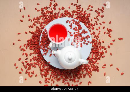 Rote getrocknete Goji-Beeren und Tasse heißen Tee auf beigem Hintergrund Stockfoto