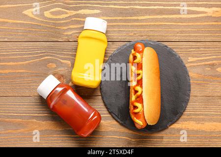 Brett mit leckerem Hot Dog, Ketchup und Senf auf hölzernem Hintergrund Stockfoto