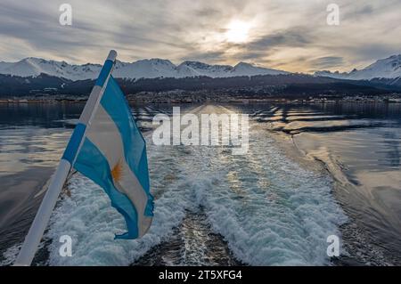 Sonnenuntergang über der Stadt Ushuaia vom Beagle Channel aus gesehen Bootsausflug mit argentinischer Flagge, Argentinien. Stockfoto