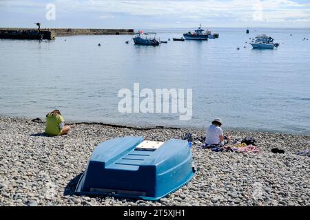 Frankreich, Omonville-la-Rogue, Le Hable, 02.09.2023: zwei Frauen sitzen auf dem Kiesstrand in der ruhigen Hafenbucht Le Hable in Omonville-la-Rogue A Stockfoto