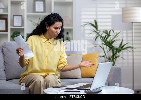 Traurig enttäuscht und verärgert unzufriedene Frau, die zu Hause Hausaufgaben macht, hispanische Frau mit lockigem Haar, die Online-Darlehen, Rechnungen und Mietverträge bezahlt, das Haushaltsbudget mit Laptop berechnet. Stockfoto