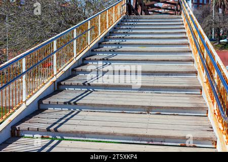 Städtische Fußgängerbrücke mit Holztreppen über einer belebten Autobahn. Die hölzernen Treppen führen die Reisenden hinauf zum zentralen Gehweg der Brücke Stockfoto