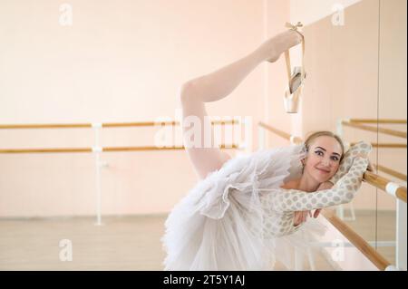 Die schöne junge Ballerina probt einen Solo-Part in einer Klasse mit einer Barre. Schlanke anmutige Tänzerin wird vor der Vorstellung engagiert. Stockfoto