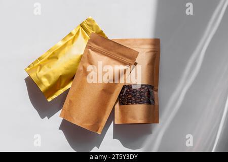 Braune Kraftpapierbeutel mit Kaffeebohnen Draufsicht mit Schatten isoliert auf weißem Hintergrund. Lebensmittelverpackung flach liegend Stockfoto