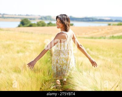 Zurück, Freiheit und Porträt der glücklichen Frau auf dem Feld im Freien im Sommer. Rückansicht, Person in der Natur und offene Arme auf dem Bauernhof, Gras und Stockfoto