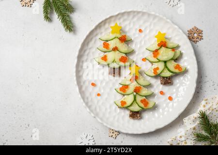 Kreative Kindersandwiches in Form eines Weihnachtsbaums mit Frischkäse und Gurke auf hellem Hintergrund, Blick von oben Stockfoto