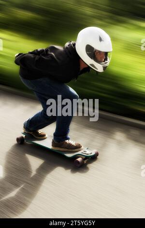 Mann, Longboard und Geschwindigkeit mit Bewegungsunschärfe auf der Straße mit Helm für Sport, Fitness und Outdoor im Sommer. Person, Skateboard und schnell auf der Straße mit Stockfoto