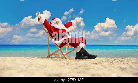 Aufregender weihnachtsmann, der einen Sommerurlaub auf einem Liegestuhl am Strand am Meer genießt Stockfoto