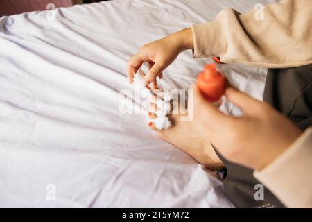 Nahaufnahme des Fußes einer jungen Frau, die zu Hause auf dem Bett Pediküre macht Stockfoto