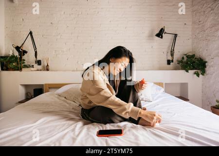 Junge chinesische, fröhliche Frau, die zu Hause Pediküre auf dem Bett macht Stockfoto