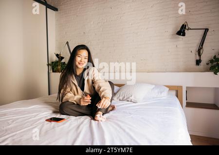 Junge chinesische, fröhliche Frau, die zu Hause Pediküre auf dem Bett macht Stockfoto