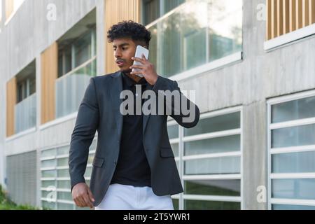 Horizontales Porträt eines abgelenkten jungen arabischen Geschäftsmannes, der auf der Straße mit dem Telefon spricht Stockfoto
