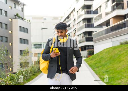 Lässiger arabischer Geschäftsmann, der ein Telefon mit Kopfhörern benutzt und auf einem Weg durch die Stadt läuft Stockfoto