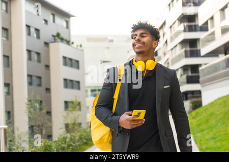 Horizontales Foto mit Kopierraum eines modernen arabischen Geschäftsmannes, der im Freien Telefon und Kopfhörer hält Stockfoto