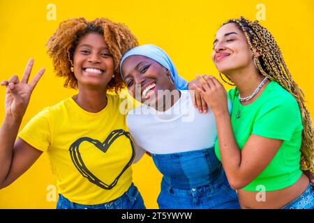 Junge Frauen mit unterschiedlichem religiösem Hintergrund, die ein Friedenszeichen mit Gesten auf gelbem Hintergrund posieren Stockfoto