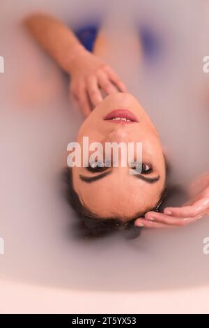 Künstlerisches Porträt einer Frau, die in einem Bad halb in milchgefülltem Wasser liegt Stockfoto