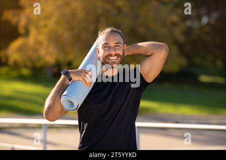 Sportlicher junger Mann mit Fitnessmatte im ruhigen Park Stockfoto