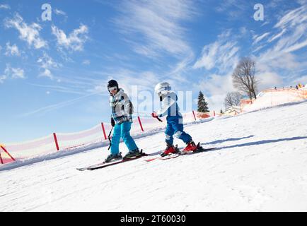 Kleiner Junge, der mit seinem Vater in den Winterferien in den schneebedeckten Bergen an einem sonnigen kalten Tag Ski fahren lernt. Aktive Winterspaziergänge mit Kindern. Saisonal Stockfoto