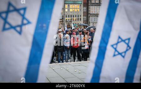 Bremen, Deutschland. November 2023. Teilnehmer einer Gedenkveranstaltung für die Opfer des Terroranschlags der Hamas auf Südisrael stehen hinter den Flaggen des Staates Israel auf dem Bremer Marktplatz. Hunderte von Menschen waren gekommen, um vor dem Bremer Parlament zu gedenken. Quelle: Focke Strangmann/dpa/Alamy Live News Stockfoto