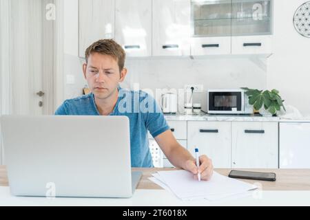 Fernunterricht, Online-Lektion. Zielgerichteter, intelligenter männlicher Student, der aus der Ferne mit einem Laptop studiert und sich während eines Online-Vortrags Notizen macht Stockfoto